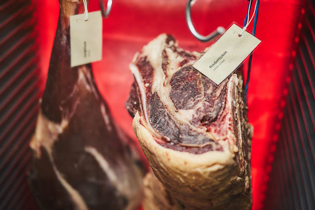 Dry-Aged Rindfleischstücke hängen in rot beleuchtetem Dry Ager Reifeschrank