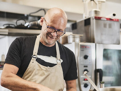 Rainer Trautenbach lächelt beim Kochen am Herd