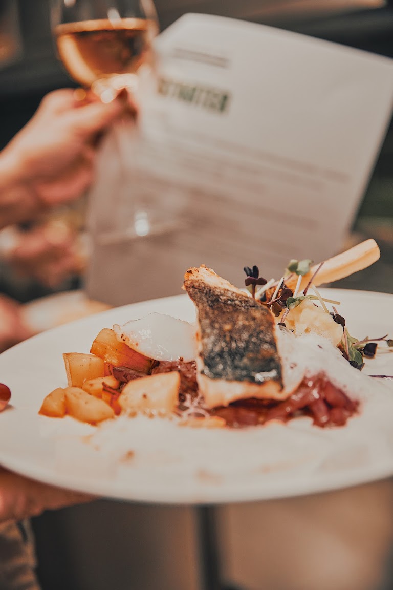 Professionell angerichteter Fischteller mit Gemüse und Sauce, gehalten neben einem Weinglas