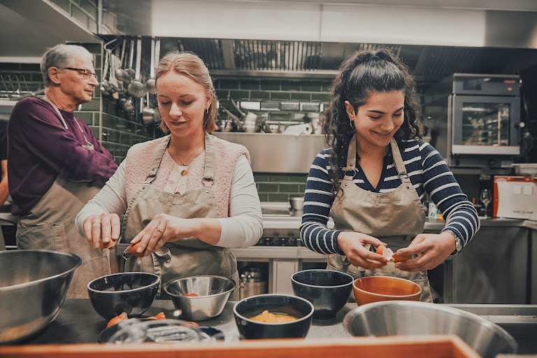 Zwei Kochkursteilnehmerinnen schlagen Eier auf und bereiten gemeinsam in der Profiküche zu