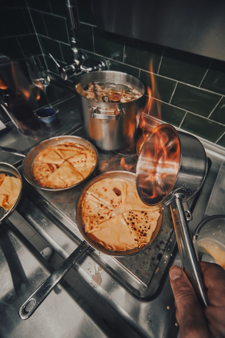 Dramatischer Moment: Flambierte Crêpes Suzette in Kupferpfanne mit offenem Feuer