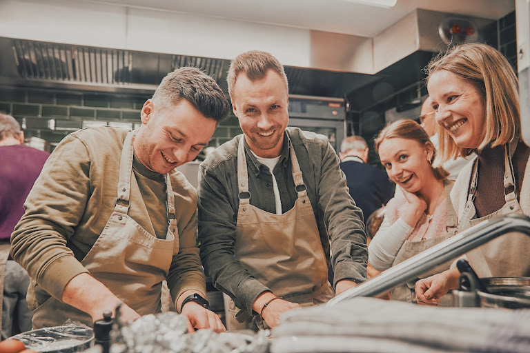 Gruppe junger Kochkursteilnehmer lacht und arbeitet gemeinsam an der Küchenstation
