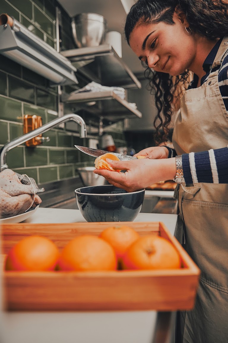 Kochkursteilnehmerin mit Schürze schneidet eine Orange in der professionellen Küche mit grünen Kacheln