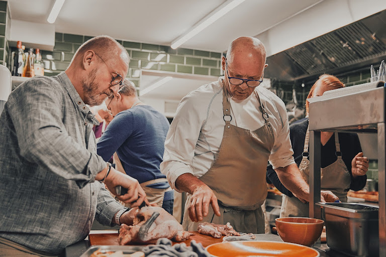 Rainer Trautenbach sieht einem Teilnehmer beim Zerteilen eines Huhns zu und greift korrigierend ein