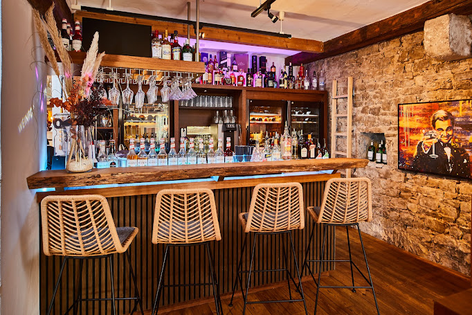 Bar mit Rattanbarhockern und historischer Steinwand in der Vinothek Weinforum Franken